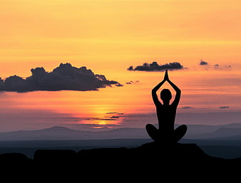 Silhouette of person meditating in yoga pose at sunset
