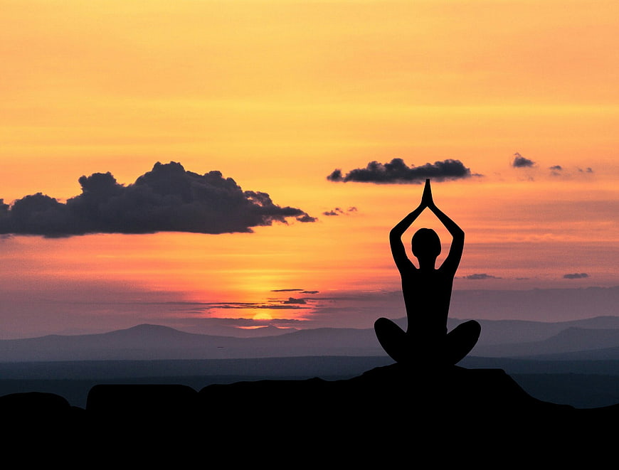 Silhouette of person meditating in yoga pose at sunset