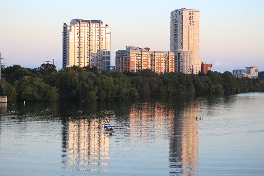 Modern apartment buildings reflecting in calm river water at sunset