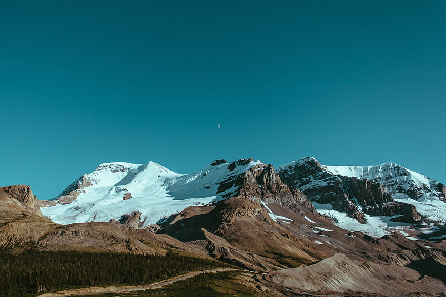 Snow-Capped Mountain Peaks Under Teal Sky with Crescent Moon