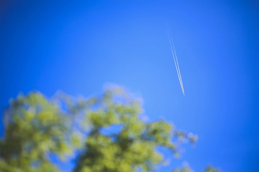 Airplane contrail in blue sky with blurred green trees