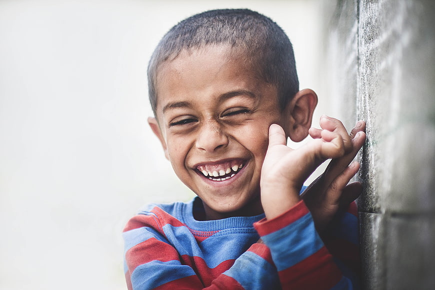 Happy young boy laughing while leaning against a wall