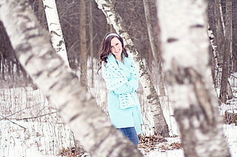 Smiling woman in aqua coat standing in snowy birch forest