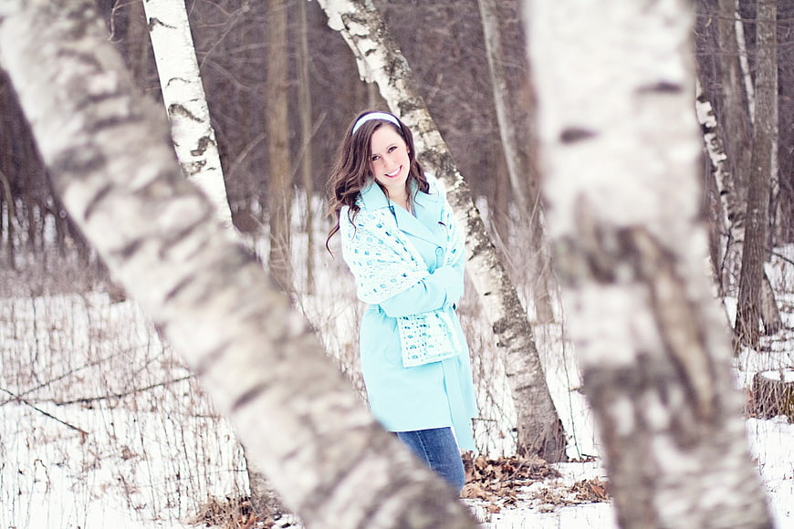 Smiling woman in aqua coat standing in snowy birch forest
