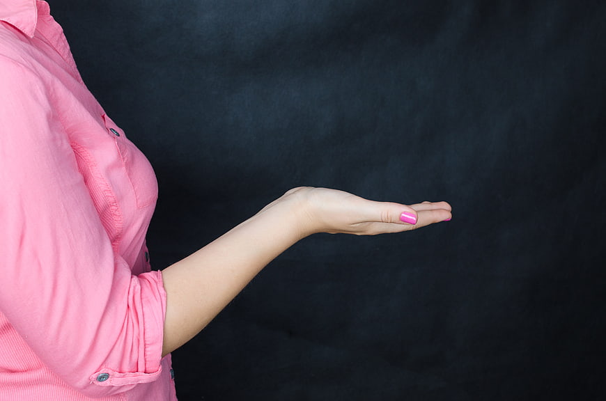 Woman in Pink Shirt Holding Out Open Palm on Dark Background