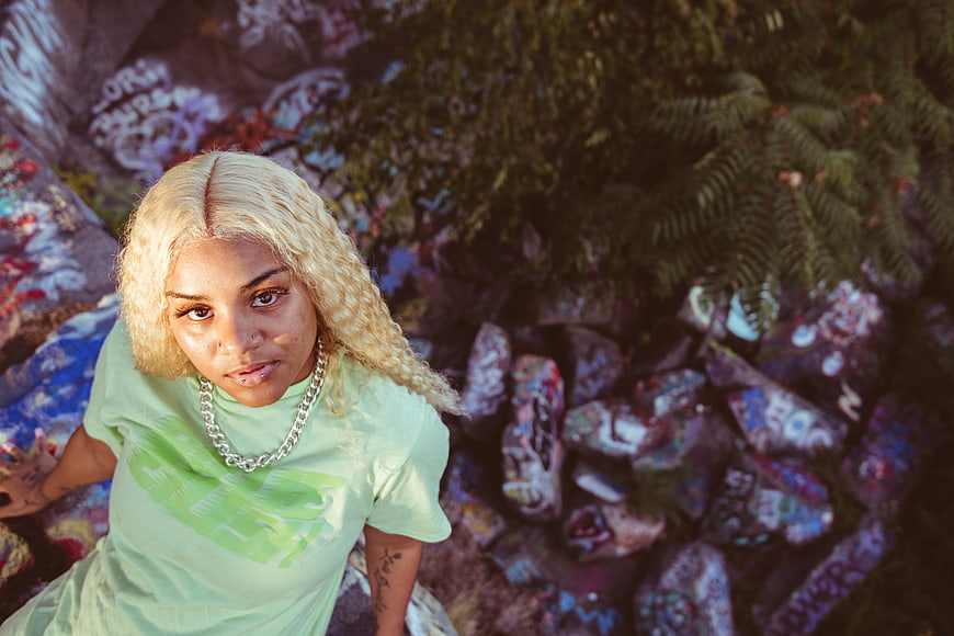 Blonde Woman in Green Shirt Looking Up at Graffiti Rocks