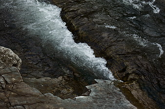 Aerial view of turbulent river rapids flowing over dark rocks