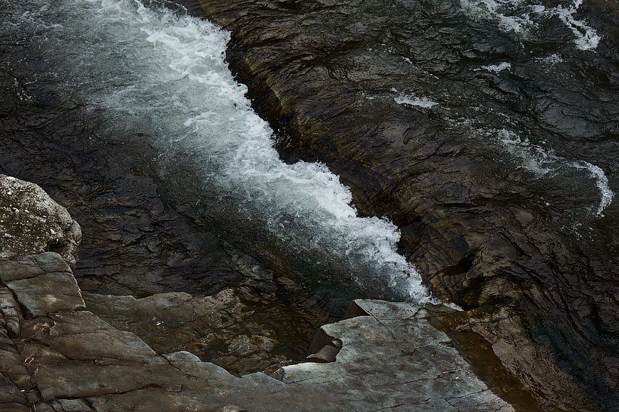 Aerial view of turbulent river rapids flowing over dark rocks