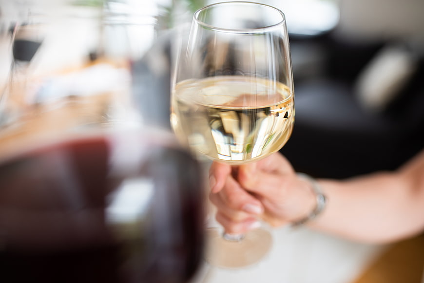 Hand holding white wine glass with red wine foreground