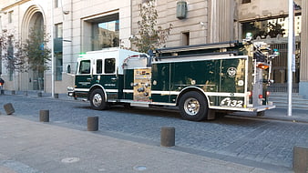 Green and white fire truck parked on cobblestone street