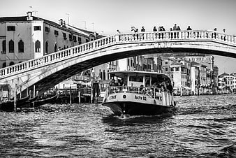 Black and white photo of water bus passing under bridge in Venice