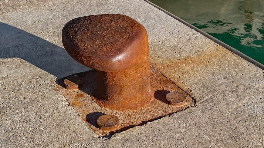 Rusty Mooring Bollard on Concrete Dock by Water