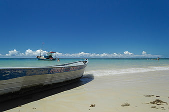 Fishing boat on white sand beach with turquoise ocean and blue sky