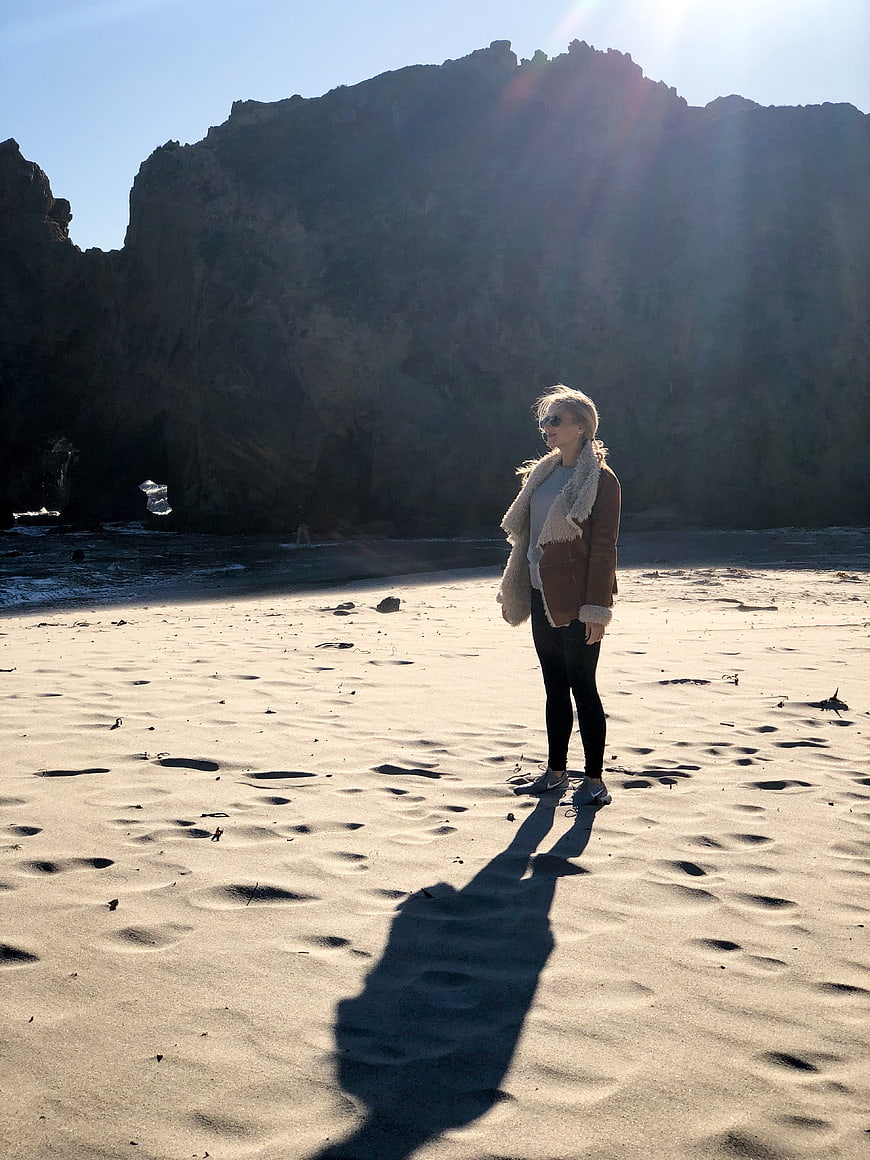 Woman standing on sandy beach with dramatic cliff backdrop