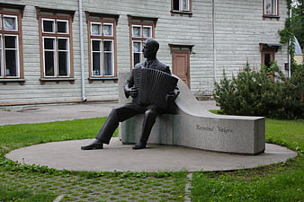 Bronze Statue of Man Playing Accordion in Front of White Wooden Building