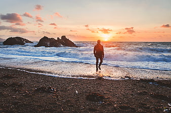 Man Walking on Rocky Beach at Sunset