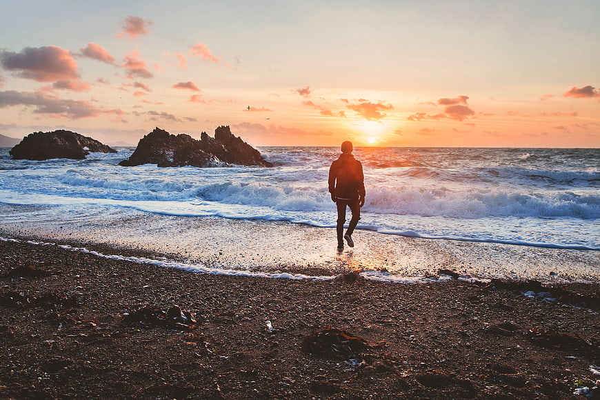 Man Walking on Rocky Beach at Sunset