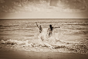 Two women jumping in ocean waves on a beach