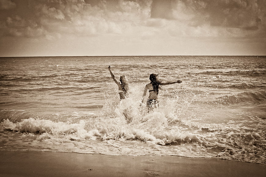 Two women jumping in ocean waves on a beach