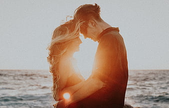Romantic couple embracing on the beach at sunset with warm backlight
