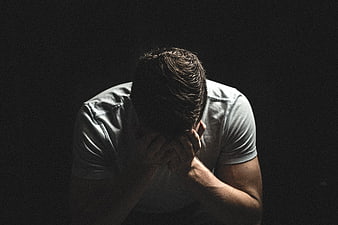 Sad man holding head in hands against dark background