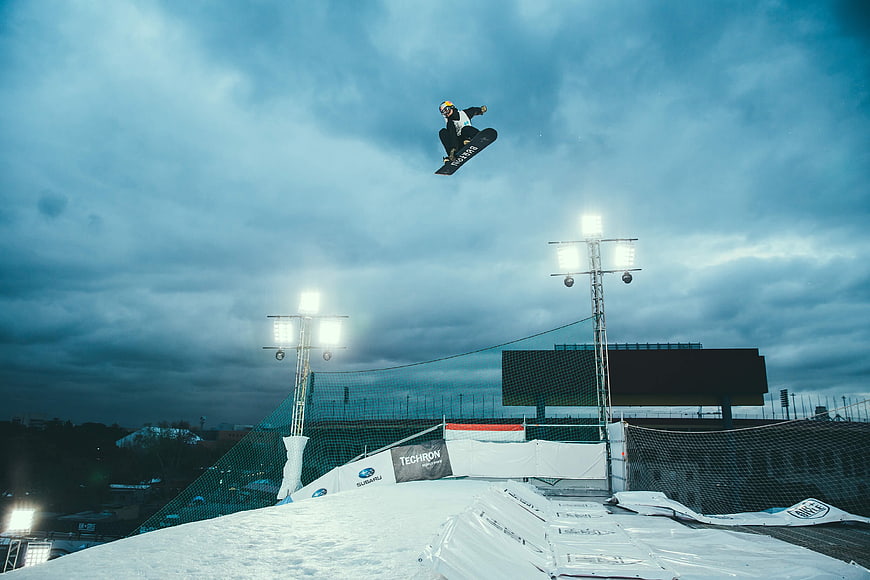 Snowboarder performing high jump at night under stadium lights