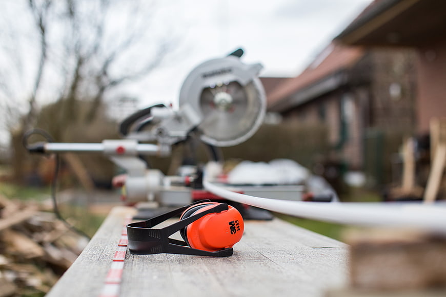 Orange ear protection on wooden plank with blurred miter saw background