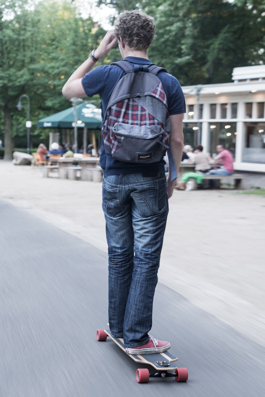 Young Man Longboarding in Park with Backpack