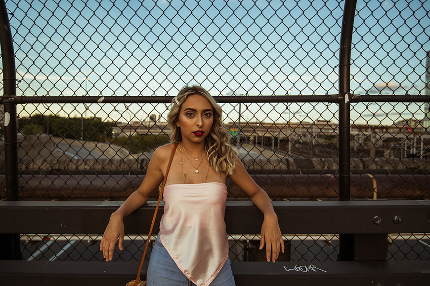 Blonde Woman in Pink Top Leaning on Urban Fence