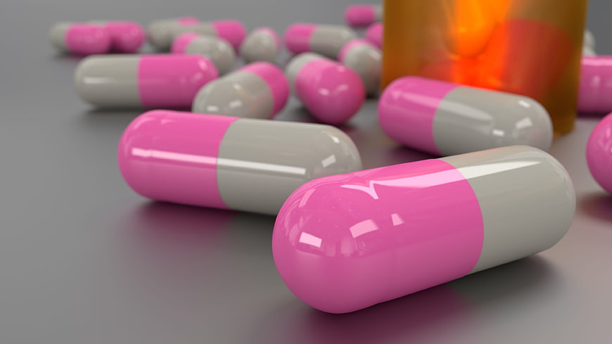 Pink and white medicine capsules with orange bottle