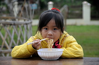 Young Asian girl eating noodles with chopsticks outdoors