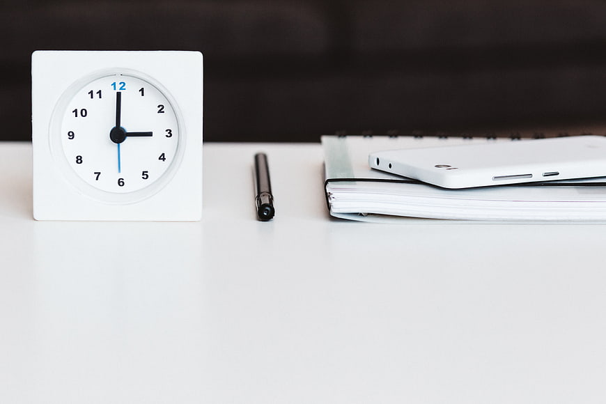 White desk clock, pen, and notebook on a clean white surface