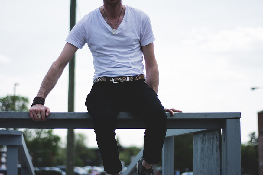 Man in White V-Neck T-Shirt and Black Pants Sitting on Railing