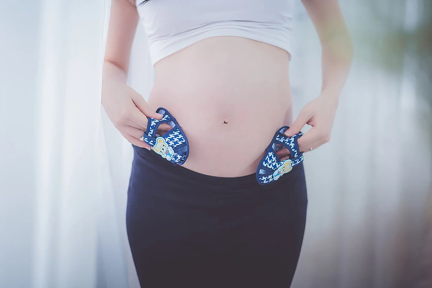 Pregnant woman holding baby shoes against belly