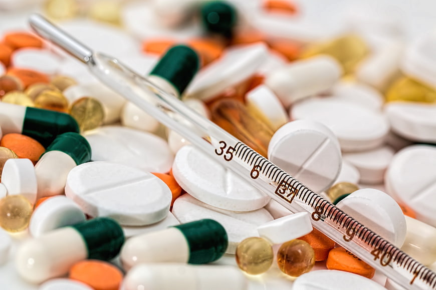 Glass thermometer on pile of assorted pills and capsules