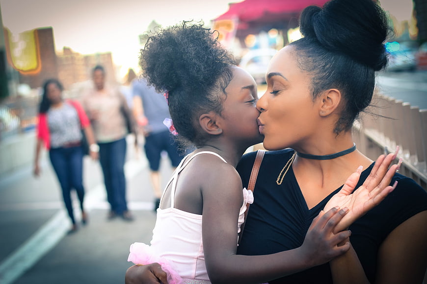 African American mother kissing daughter on cheek outdoors
