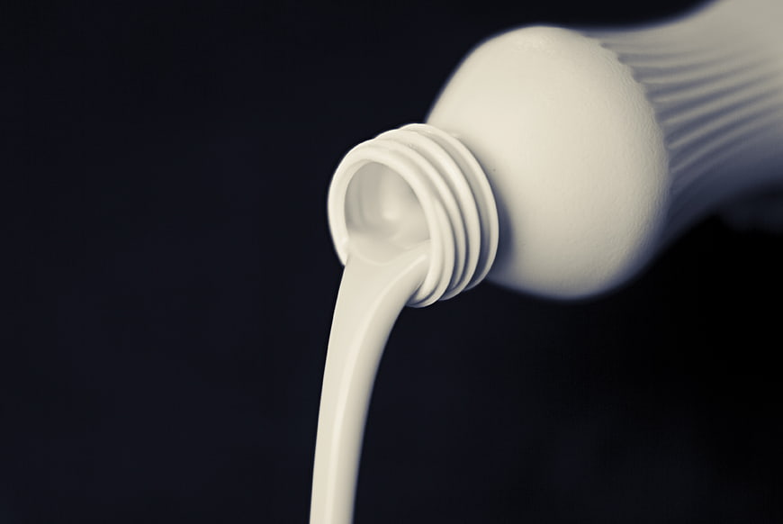 White liquid pouring from a bottle against a dark background