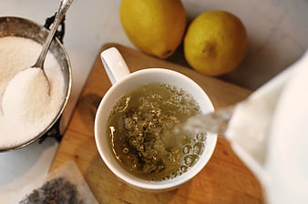 Overhead view of hot water pouring into a cup of green tea with lemons and sugar