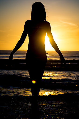 Silhouette of Woman Walking on Beach at Sunset