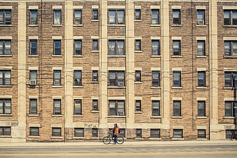 Cyclist Riding Past Brick Apartment Building Facade