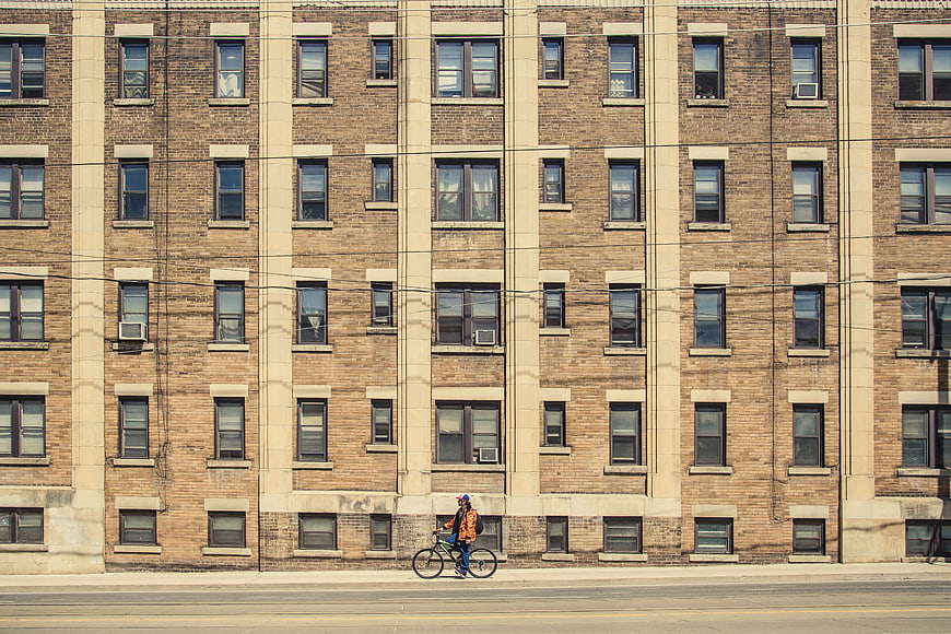 Cyclist Riding Past Brick Apartment Building Facade