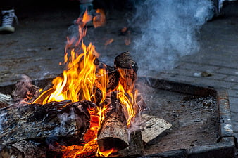 Close-up of burning logs in a metal fire pit with smoke