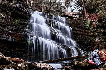 Photographer capturing long exposure waterfall in forest
