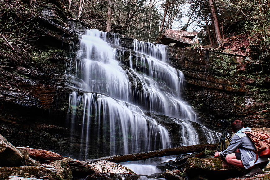 Photographer capturing long exposure waterfall in forest