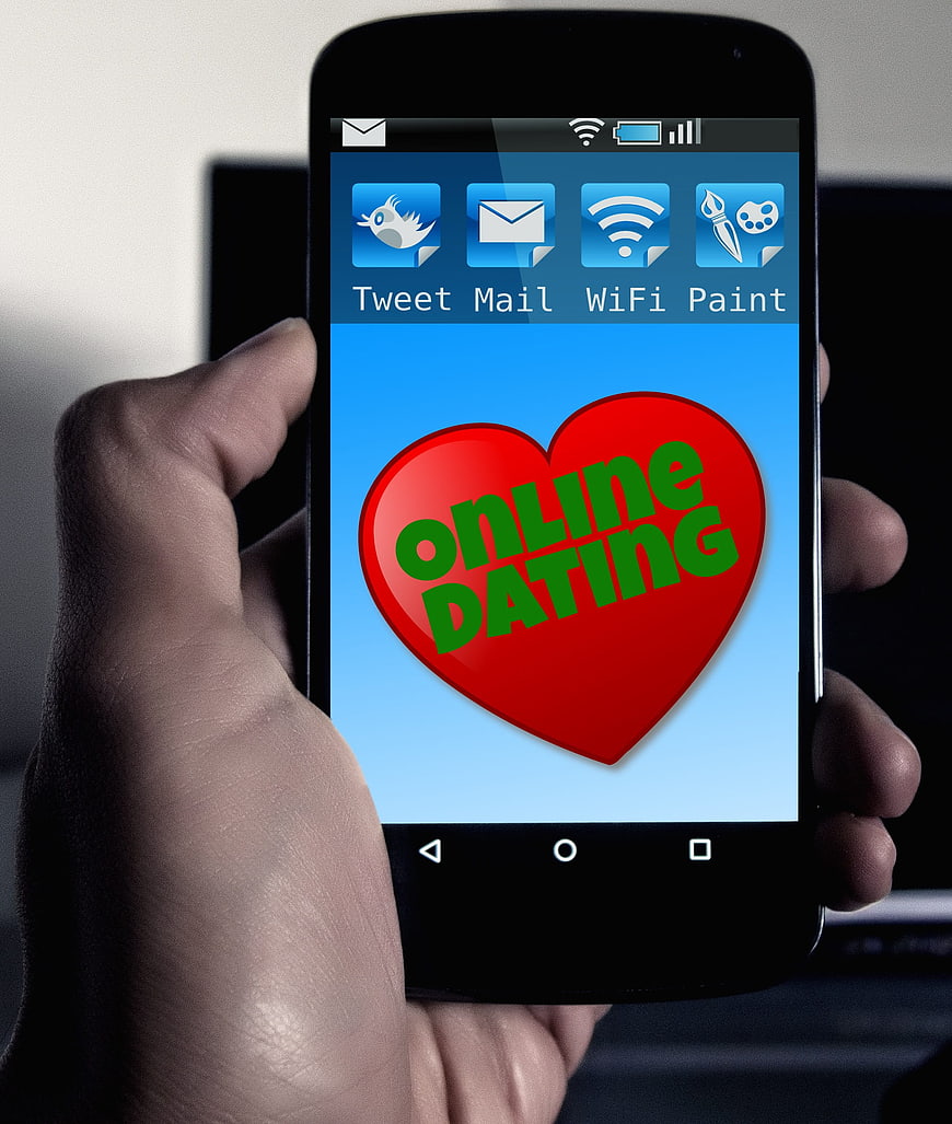 Hand holding smartphone displaying online dating app with red heart icon
