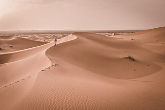 Lone figure walking on vast desert sand dunes with footprints