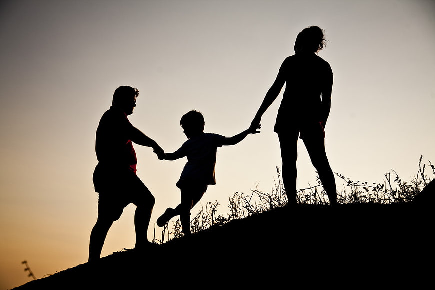 Silhouette of family playing on grassy hill at sunset