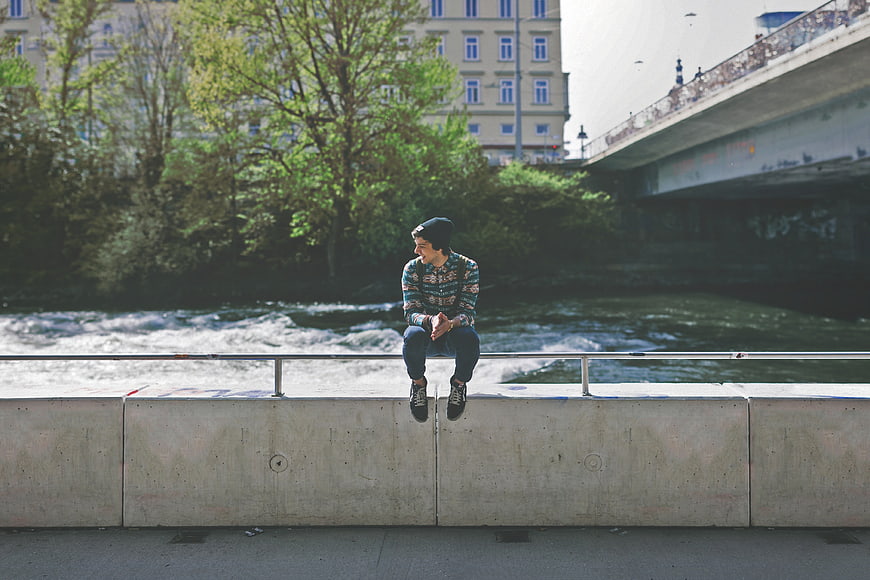 Young man sitting on concrete ledge by river