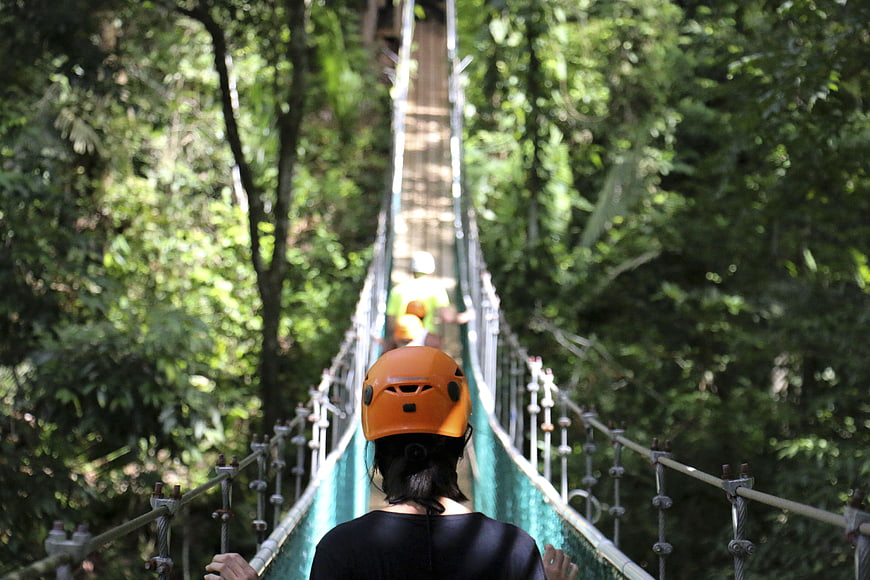 Woman in orange helmet walking on suspension bridge in forest