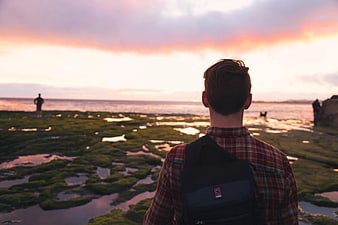 Man with Backpack Watching Sunset Over Mossy Coastline